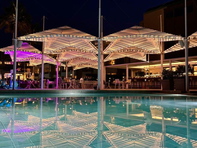 Bar de piscine éclairée avec parasols et reflet dans la piscine la nuit
