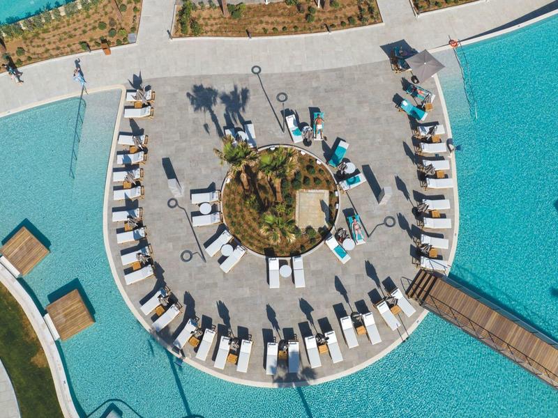Vue aérienne d'une piscine autour d'une terrasse circulaire avec des chaises longues.