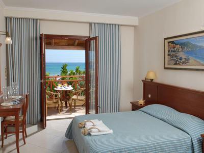 Helles Hotelzimmer mit Doppelbett, Holzmöbeln, Terrasse und Meerblick.