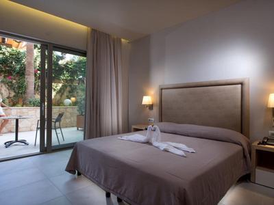 Modernes Hotelzimmer mit Doppelbett, brauner Bettdecke, Nachttischlampen und Terrasse mit Sitzbereich.