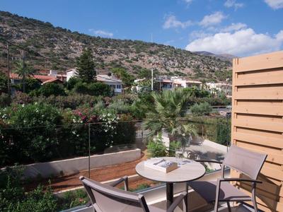 Balkon mit Tisch und Stühlen, grüner Garten und hügelige Landschaft im Hintergrund.