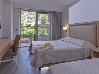 Modern eingerichtetes Hotelzimmer mit zwei Betten, Schreibtisch, Stuhl und großer Fensterfront zur Terrasse.