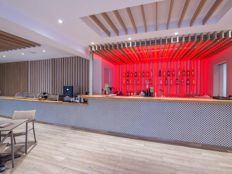 Bar d'hôtel moderne avec mur arrière éclairé en rouge, long comptoir et poutres en bois.