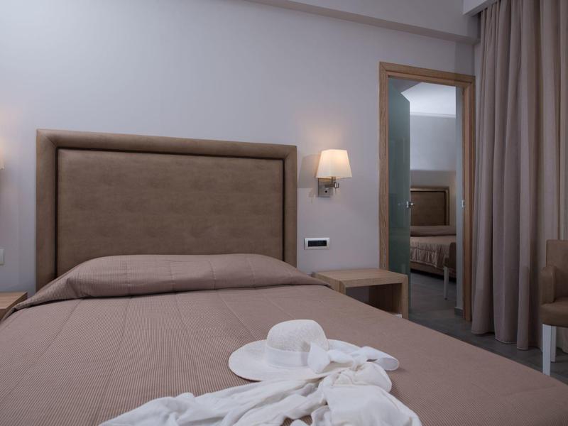 Chambre d'hôtel confortable avec un lit beige, un éclairage doux et un miroir reflétant la chambre.