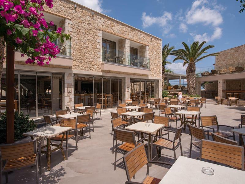 Terrasse extérieure d'hôtel avec tables et chaises en bois sous un ciel clair et un palmier.