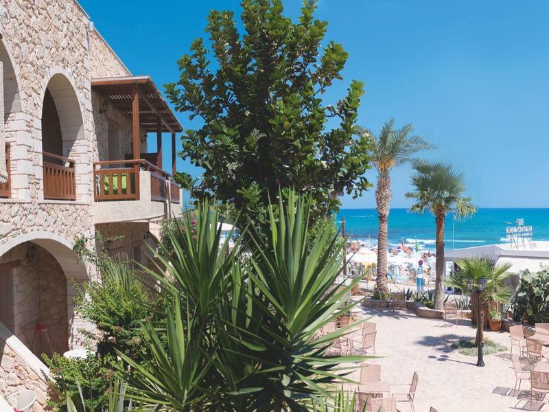 Hôtel en bord de mer avec arches en pierre, plantes vertes, vue sur la plage et le ciel bleu.
