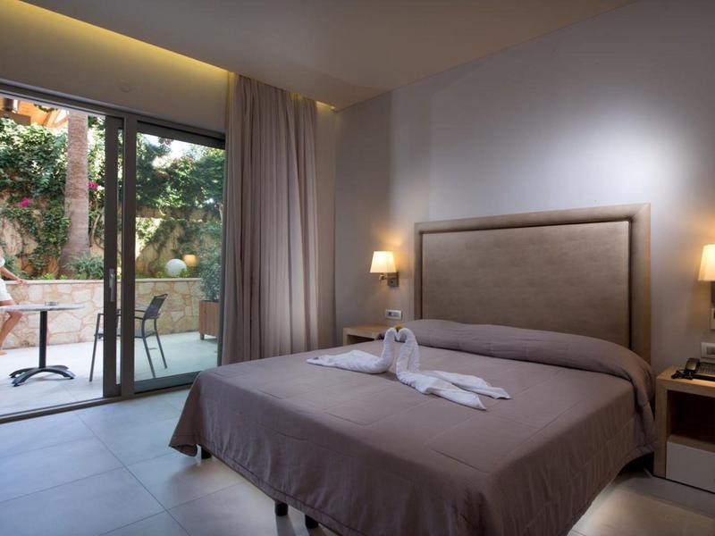 Chambre d'hôtel confortable avec lit double, lampes de chevet et porte patio donnant sur une terrasse.