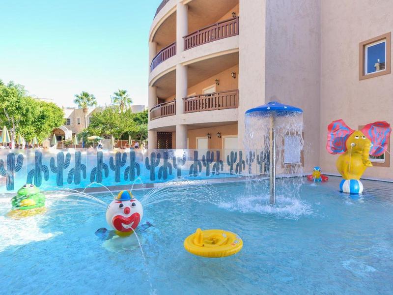Zone de piscine d'hôtel avec jouets d'eau colorés et zone de jeux peu profonde pour enfants.