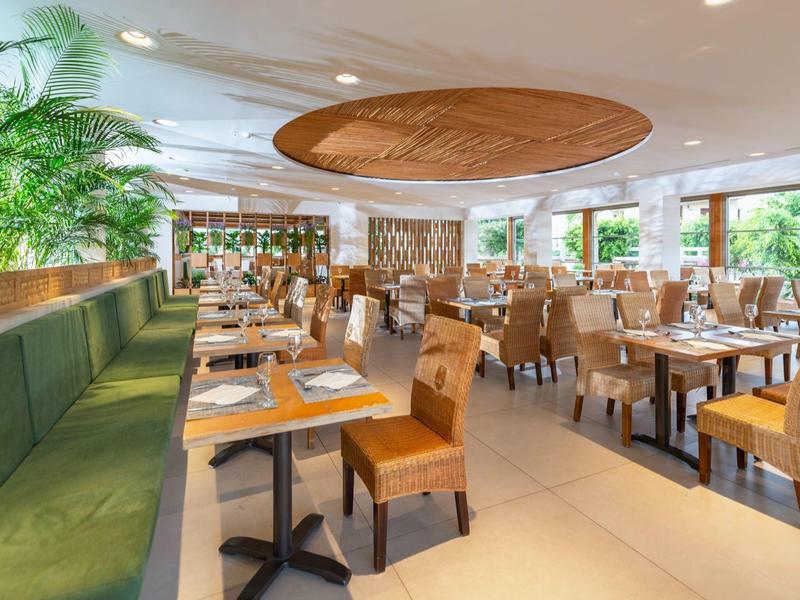 Restaurant d'hôtel spacieux avec sièges verts rembourrés et chaises en bois près de grandes fenêtres.