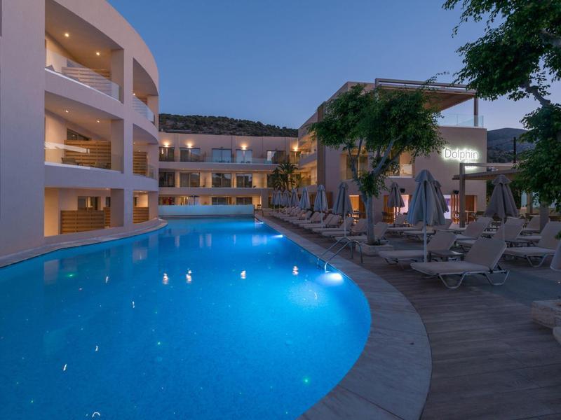 Piscine extérieure incurvée avec chaises longues et bâtiment hôtelier éclairé au crépuscule.