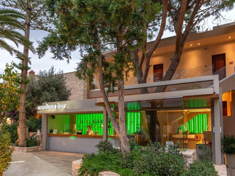 Terrasse d'hôtel moderne avec éclairage vert sous les arbres au crépuscule.