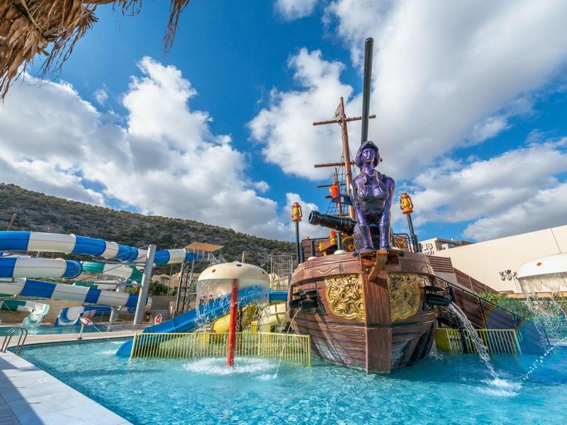 Parc aquatique extérieur avec aire de jeux sur le thème du navire pirate et toboggans sous un ciel bleu.