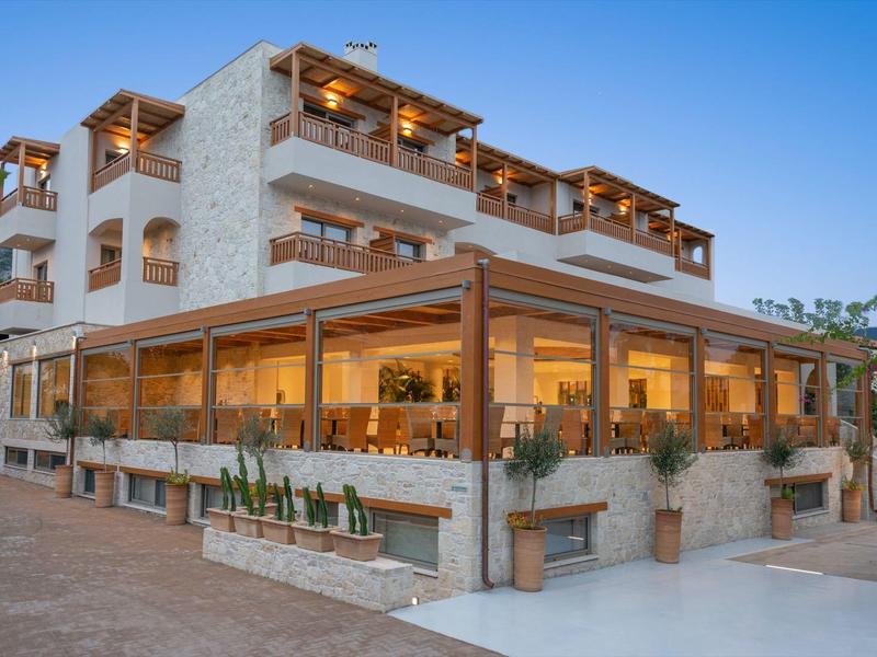 Hôtel moderne en pierre avec grandes fenêtres en verre et terrasse sous éclairage chaleureux au crépuscule.