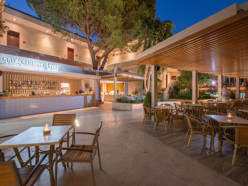 Espace repas extérieur d'hôtel avec tables et chaises en bois sous une pergola au crépuscule.