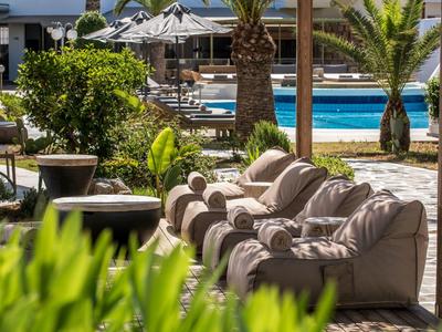 Bequeme, weiße Stühle und Tische stehen neben einem blauen Pool unter Palmen bei Sonnenschein.