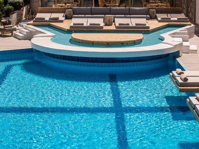 Moderner Pool mit klarem, blauem Wasser, weißen Liegen und drei runden Holzplattformen.