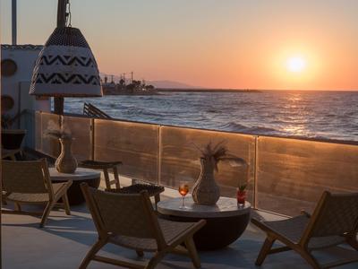 Terrassenbereich mit Stühlen, Tischen und Laternen bei Sonnenuntergang am Meer.