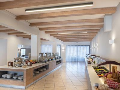 Área de buffet luminosa con diferentes alimentos, vigas de madera y suelo de baldosas en un hotel.