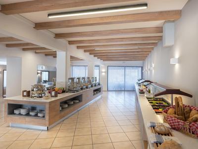 Moderne Kantine mit Buffet, hellem Holz, weißen Wänden und großem Fenster am Raumende.