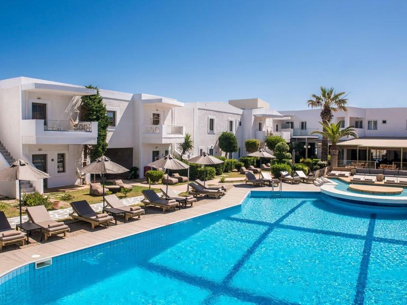 Moderno complejo hotelero con piscina azul, tumbonas y cielo claro azul.