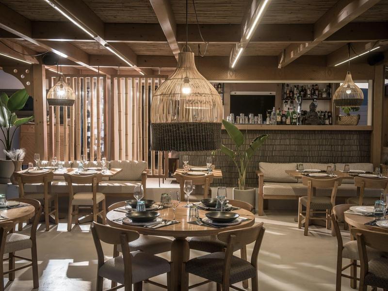 Interior moderno de restaurante con muebles de madera, luz cálida y plantas decorativas.