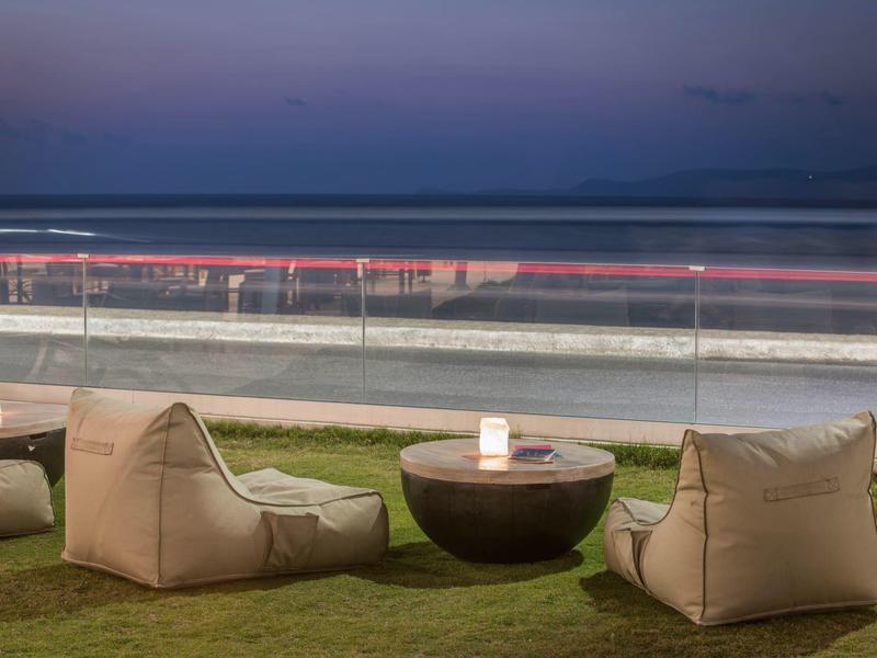 Tres puf cómodos y una mesa redonda sobre césped con vista al mar al anochecer