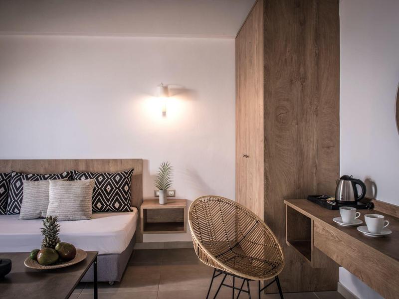 Habitación de hotel moderna amueblada con sofá, espejo de madera y silla de mimbre en tonos cálidos.