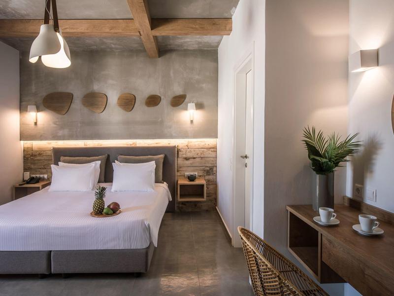 Habitación de hotel moderna con cama doble, techo de madera, mesas de noche y escritorio con planta y taza.