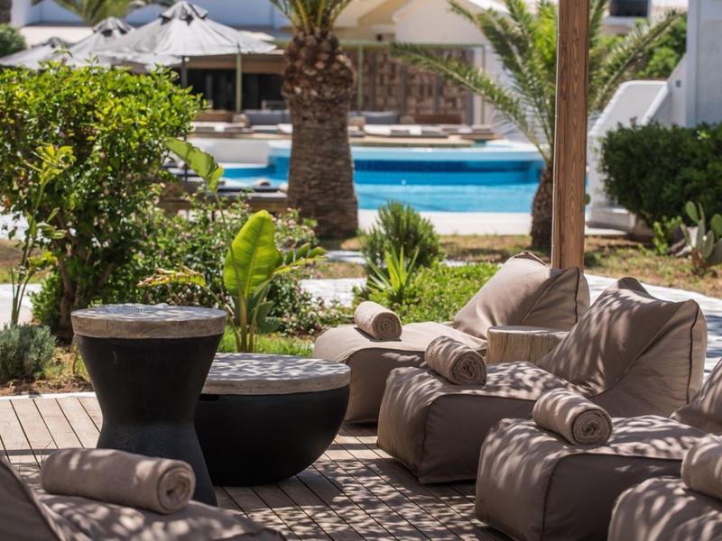 Área cómoda con cojines y piscina al fondo en un complejo hotelero.