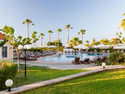 Hotelpool mit Sonnenliegen, Sonnenschirmen und Palmen bei klarem Himmel.