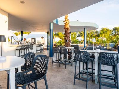 Moderní venkovní bar s židlemi a stoly pod zastíněnou střechou.