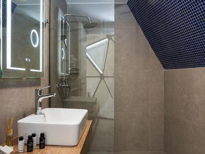 Nowoczesna łazienka z umywalką, drewnianą półką i prysznicem typu walk-in z szklaną ścianką.