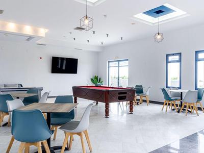 Světlá společenská místnost s kulečníkovým stolem, několika stoly a moderními židlemi