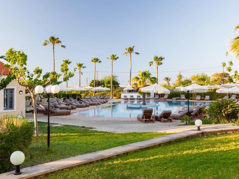 Basen hotelowy z leżakami, parasolami i palmami pod czystym niebem.