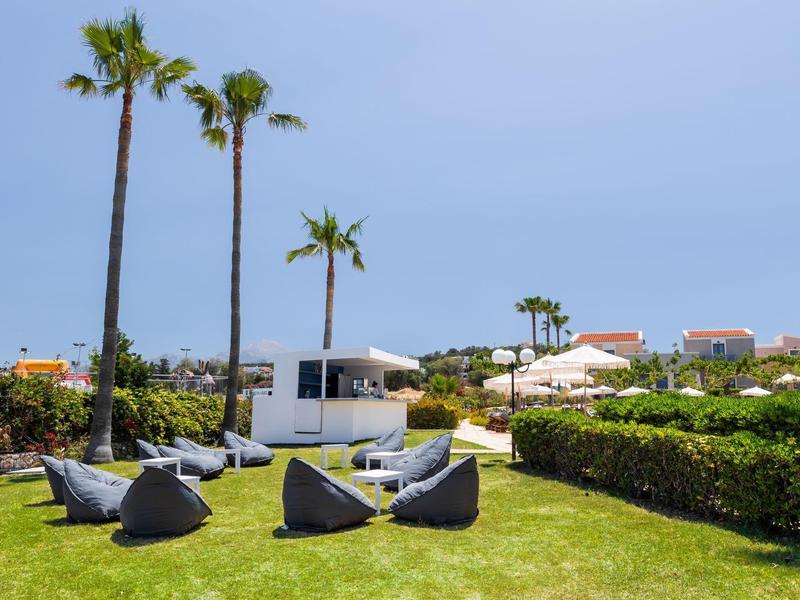 Zielony ogród z palmami i nowoczesnym miejscem do siedzenia przed domkami wakacyjnymi pod bezchmurnym niebem.