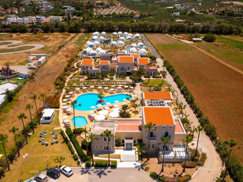 Widok z lotu ptaka ośrodka z basenem, budynkami, otoczonego polami i drzewami.