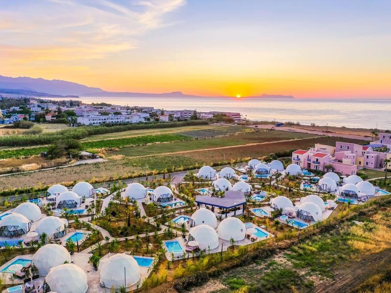 Krajobraz z białymi kopułowymi domami i polami o zachodzie słońca przy morzu.