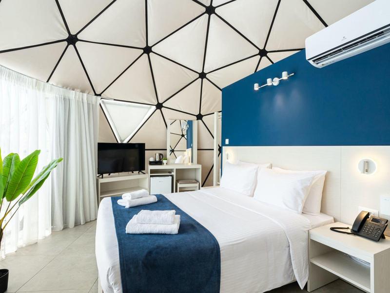 Nowoczesny pokój hotelowy w niebiesko-białym kolorze z dużym łóżkiem i roślinami przy dużym oknie.