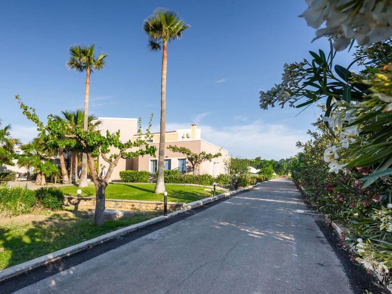 Długa asfaltowa ścieżka prowadzi przez tropikalny ogród do budynku hotelu pod niebieskim niebem.