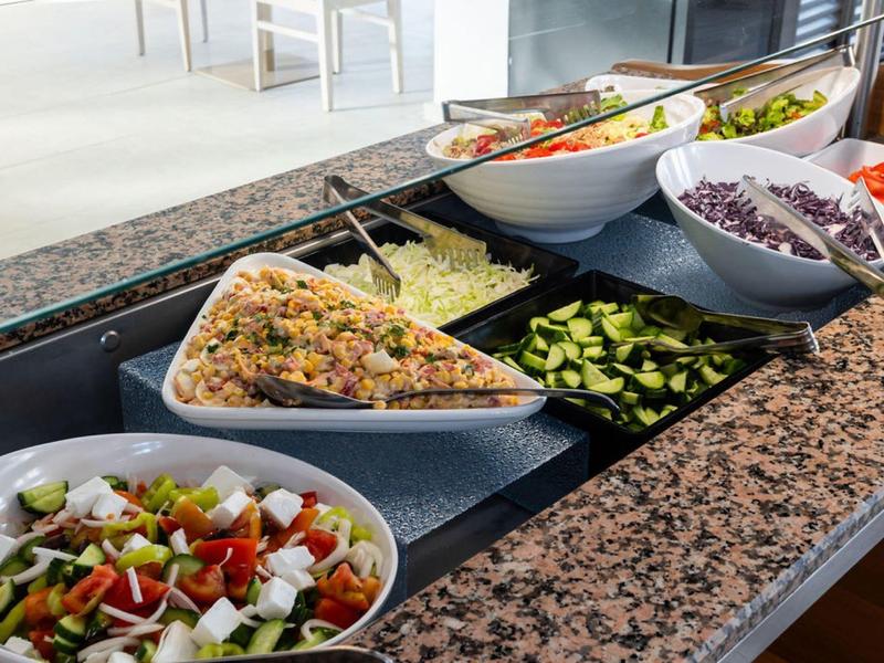 Bufet sałatkowy z różnymi świeżymi warzywami i składnikami na granitowym blacie.