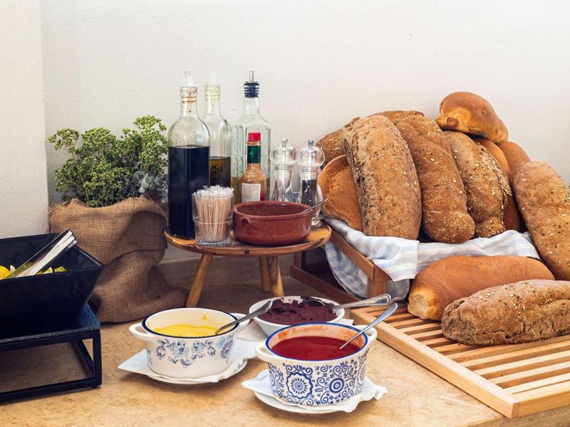 Różne rodzaje pieczywa, sosy i zioła ułożone na rustykalnym stole śniadaniowym.