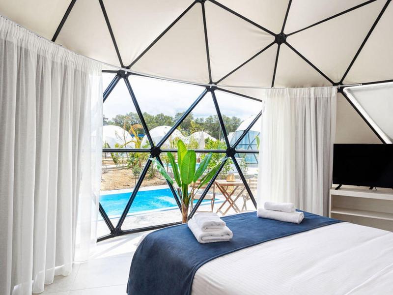 Nowoczesny pokój hotelowy z trójkątnymi oknami, widokiem na basen i krajobraz, białe zasłony.