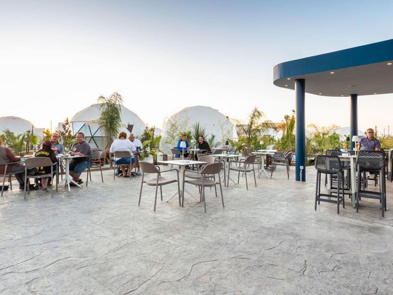 Taras z stołami i krzesłami obok namiotów kopułowych w hotelu o zachodzie słońca.