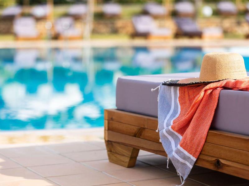 Leżak z ręcznikiem i kapeluszem przeciwsłonecznym przy basenie hotelowym.