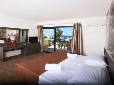 Helles Hotelzimmer mit zwei Betten, Schreibtisch und Balkon mit Meerblick.