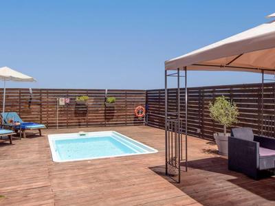 Terrasse d'hôtel moderne avec petite piscine, transats et coin salon sous des parasols.