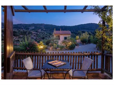 Przytulny balkon z dwoma krzesłami i stołem z widokiem na zalesione wzgórza i dom o zmierzchu.