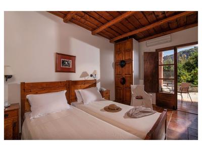 Gemütliches Zimmer mit zwei Einzelbetten, Holzdecke und offener Tür zur Terrasse im Sonnenschein.