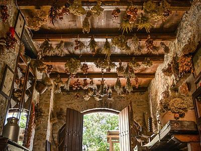 Rustykalny pokój z drewnianym sufitem i wiszącymi ziołami, widok przez otwartą arkadę na ogród.