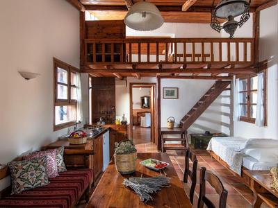 Gemütlicher Wohnbereich mit Holzmöbeln, Treppe zu einer Galerie und großen Fenstern.